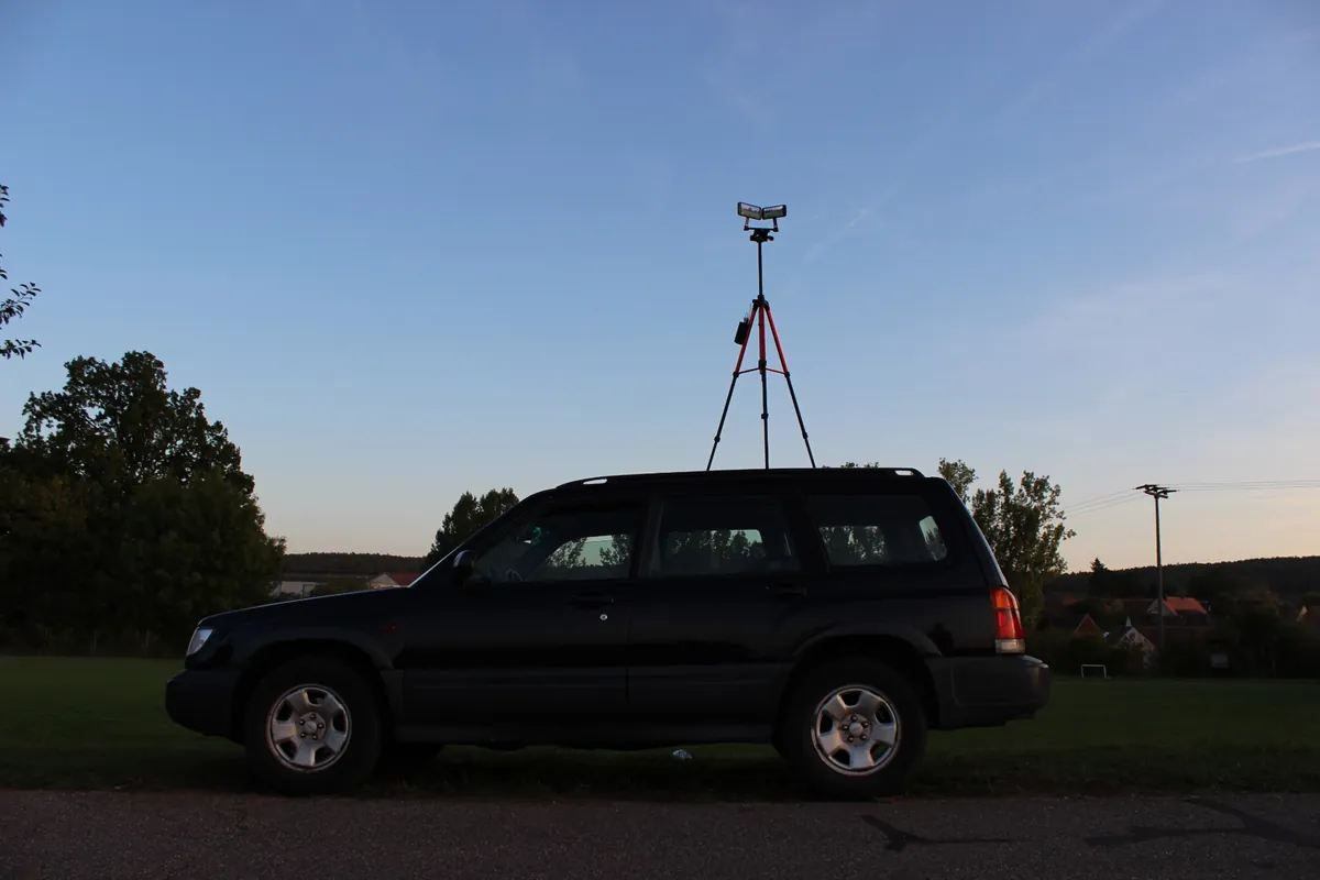 Das Stativ steht hinter einem Geländewagen und ragt mit den beiden iPhones deutlich über das Autodach.